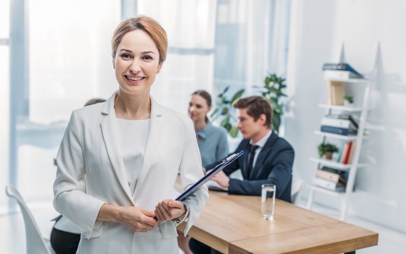 selective-focus-of-cheerful-recruiter-standing-with-clipboard-near-coworkers.jpg